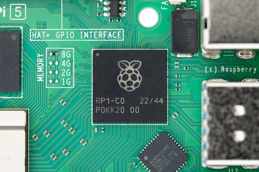 Close-up photo of part of the Raspberry Pi 5 board, centring the RP1 chip, on which the Raspberry Pi logo and text identifying the chip are printed